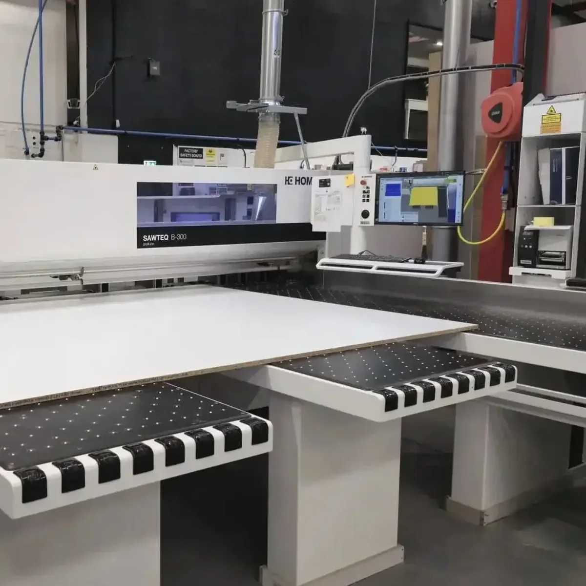 A large white panel being loaded onto the beam saw tables